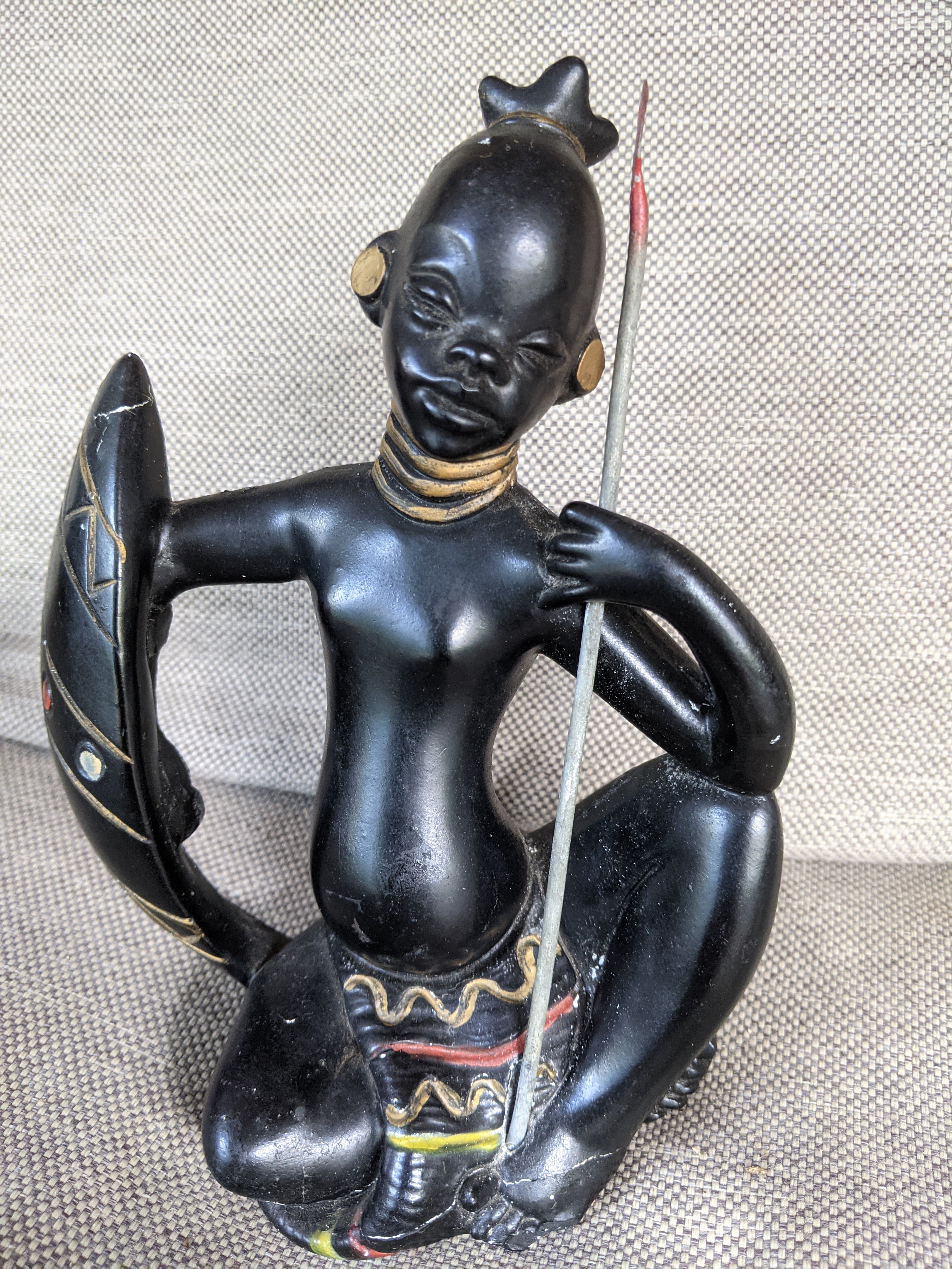 Seated warrior figurine made of chalkware holding a spear and shield