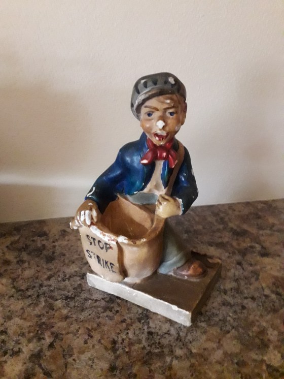 STOP STRIKE writing on a basket held by small boy figurine made of chalkware set on a rectangular base