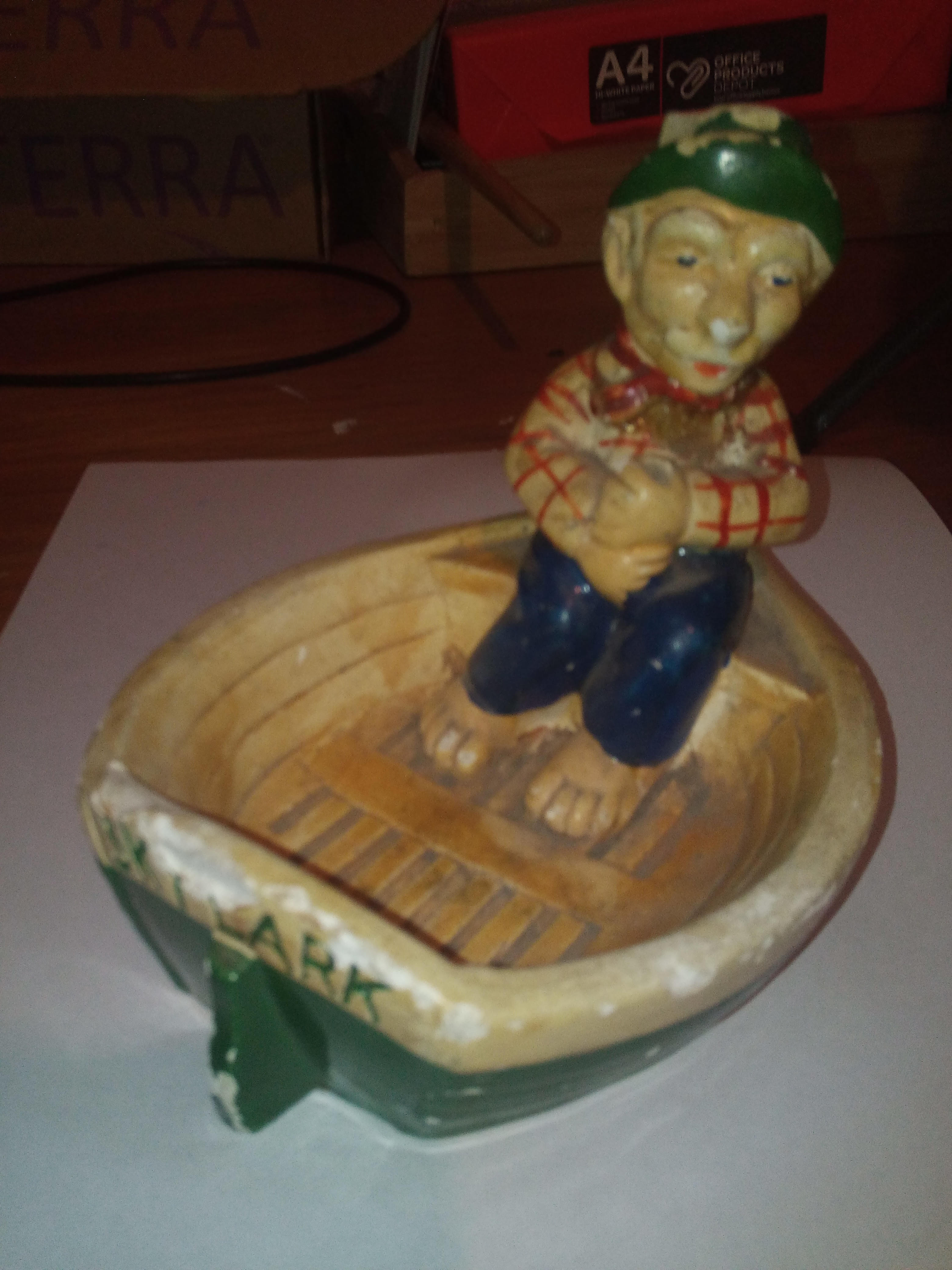 Old man with blue trousers and green hat on a small boat chalkware figurine