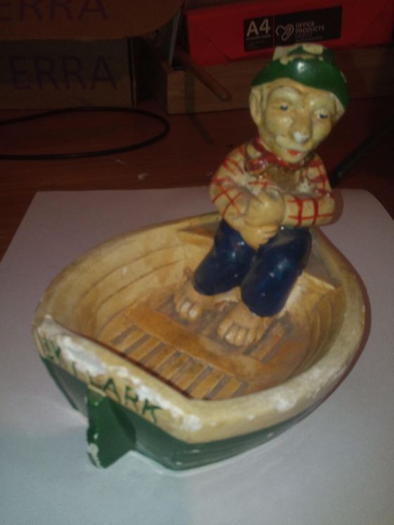 Old man with blue trousers and green hat on a small boat chalkware figurine